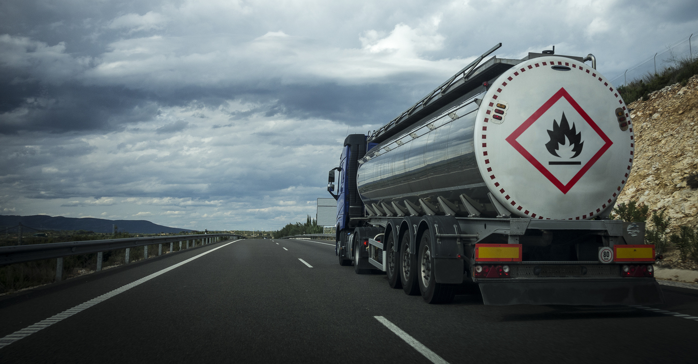 Tanker truck transporting flammable substances on a highway under a cloudy sky.